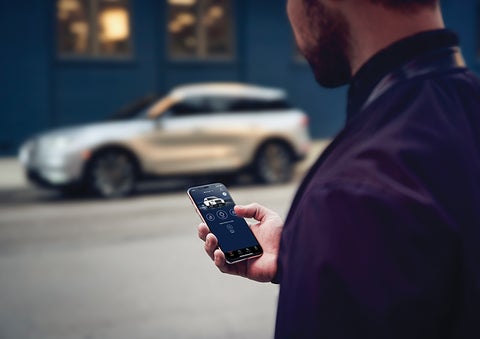 A person is shown interacting with a smartphone to connect to a Lincoln vehicle across the street. | Don Franklin Lincoln Elizabethtown in Elizabethtown KY