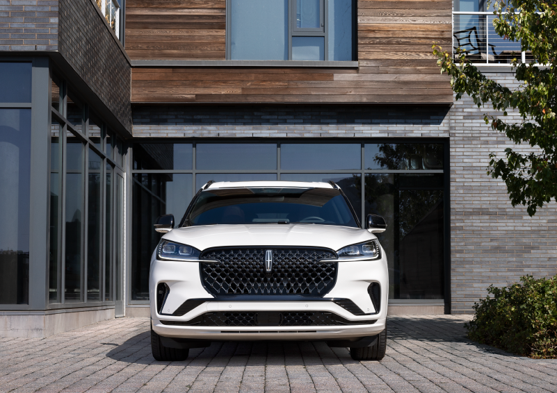 A white 2025 Lincoln Aviator® SUV is shown parked outside a modern building with gray brick and wood accents. | Don Franklin Lincoln Elizabethtown in Elizabethtown KY