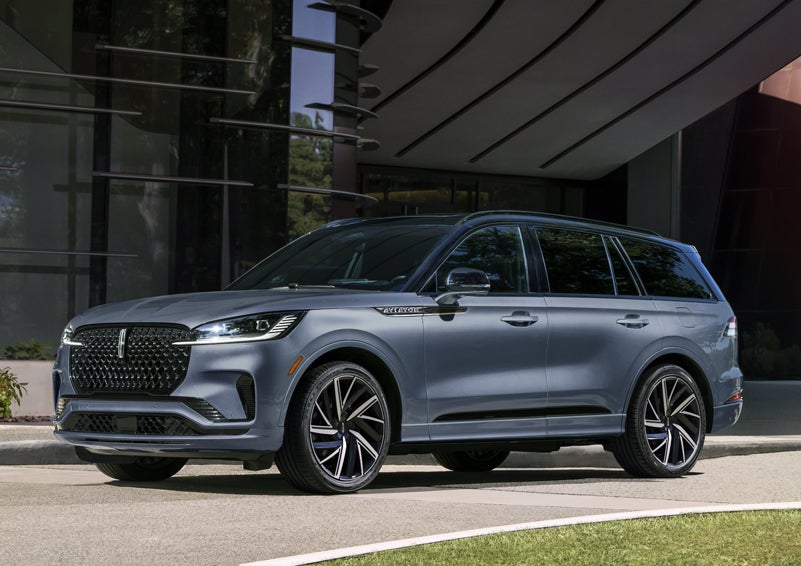 A gray 2025 Lincoln Aviator® SUV is parked outside a modern building showcasing the driver’s side of the vehicle. | Don Franklin Lincoln Elizabethtown in Elizabethtown KY