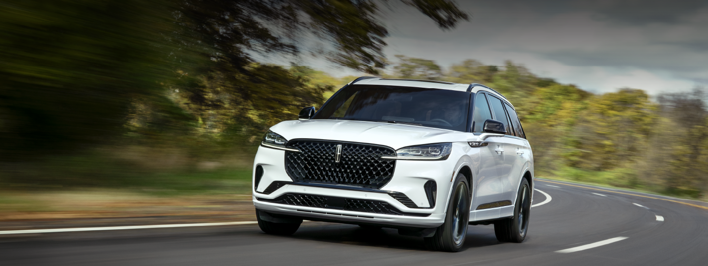 A white 2025 Lincoln Aviator® SUV is being driven down a road lined with trees. | Don Franklin Lincoln Elizabethtown in Elizabethtown KY