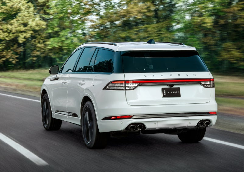 A white 2026 Lincoln Aviator® SUV is being driven away down a road lined with colorful trees. | Don Franklin Lincoln Elizabethtown in Elizabethtown KY
