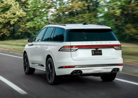 A white 2026 Lincoln Aviator® SUV is being driven away down a road lined with colorful trees. | Don Franklin Lincoln Elizabethtown in Elizabethtown KY