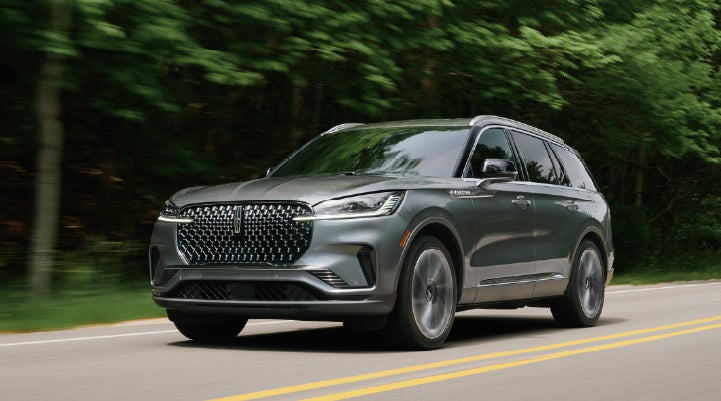 A 2027 Lincoln Aviator® SUV is being driven down a road lined with trees. | Don Franklin Lincoln Elizabethtown in Elizabethtown KY
